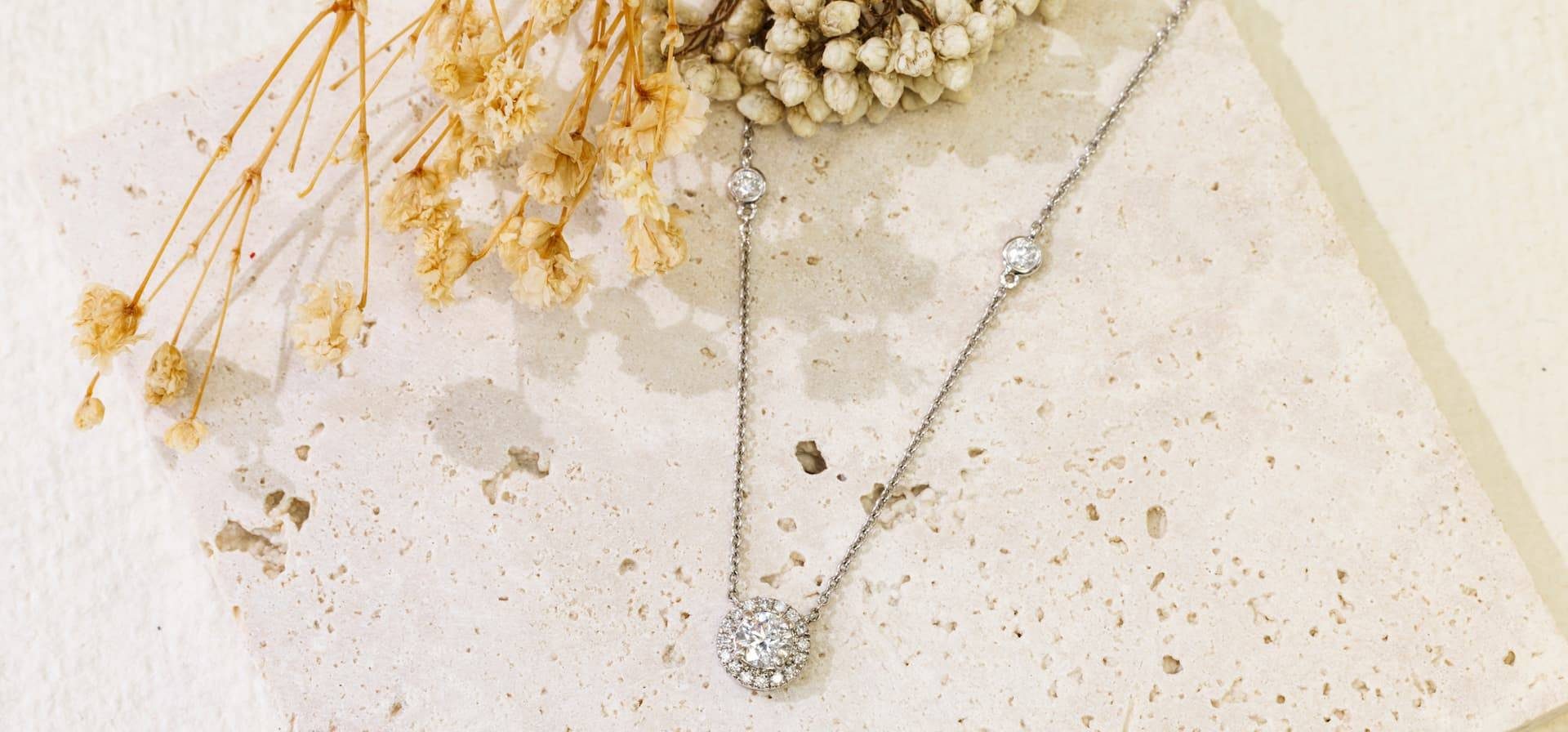 Halo solitaire diamond necklace from Spencer Morgan Jewellers on travertine with dried flowers